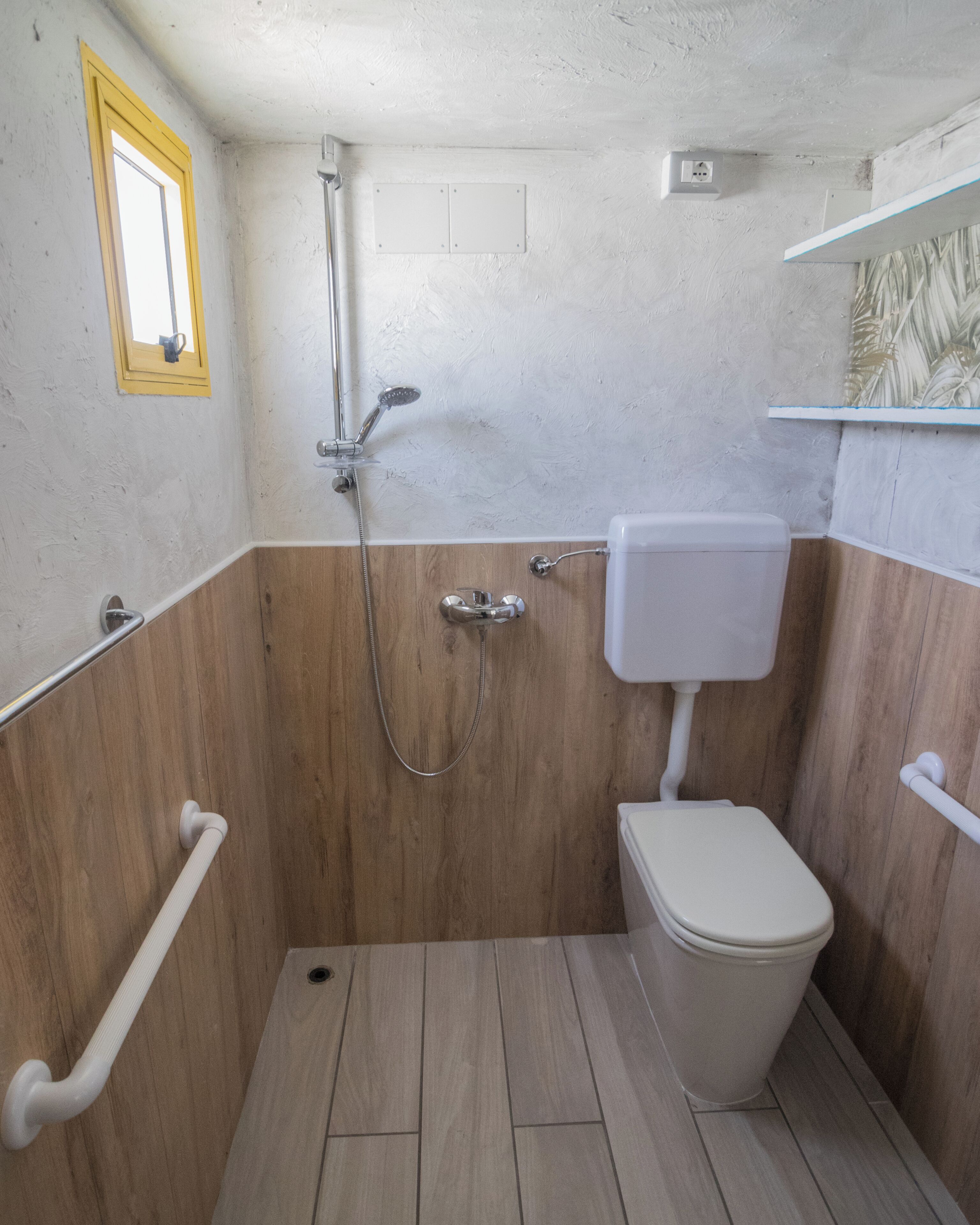 Une petite salle de bain avec douche, toilettes et lambris en bois.
