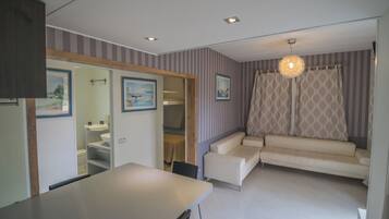 A modern living room with a sofa, a dining table, and a kitchen area visible through an open door.
