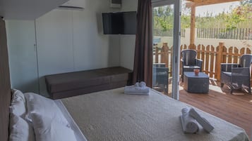 A hotel room with a large bed, a flat-screen TV, a bench, and a patio area with wicker furniture.