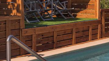 Una piscina con muelle de madera, una escalera metálica y una sombrilla roja.