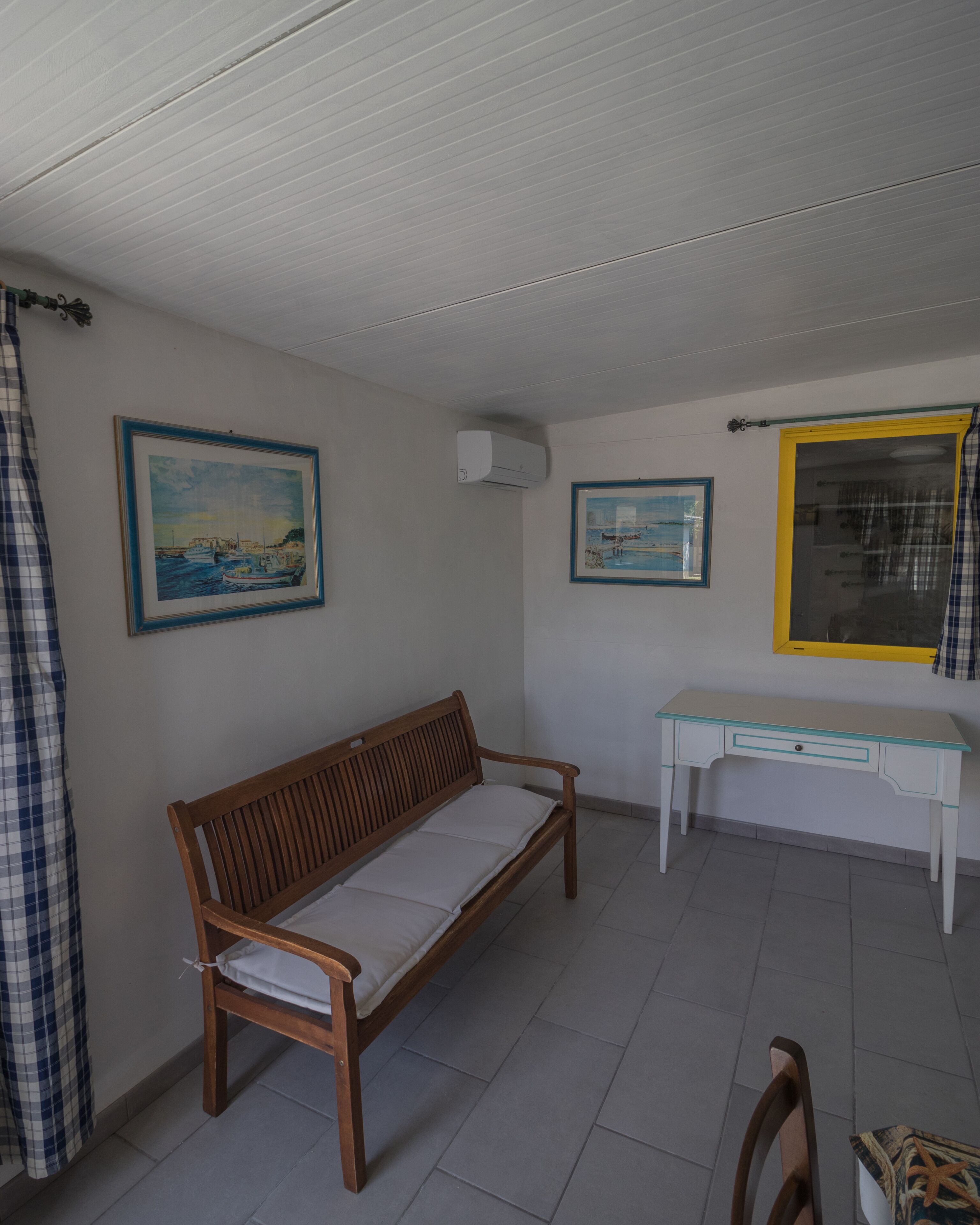 A room with a wooden bench, a white desk, and two framed paintings on the walls.