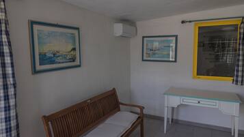A room with a wooden bench, a white desk, and two framed paintings on the walls.