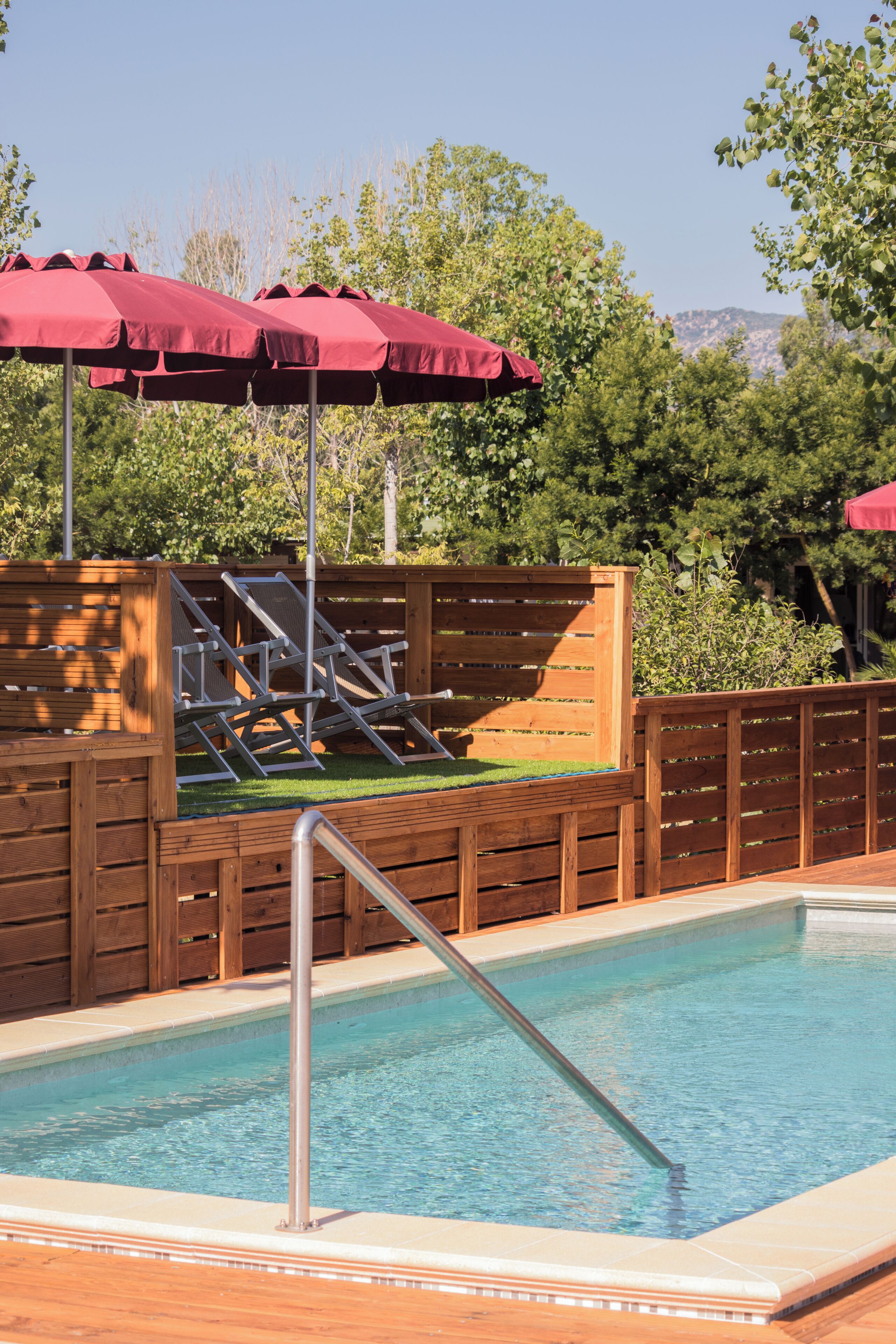 A swimming pool with wooden deck, metal ladder, and red umbrellas.