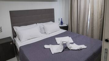 A neatly made bed with a gray headboard, a bedside table with a bottle, and a curtain on the window.