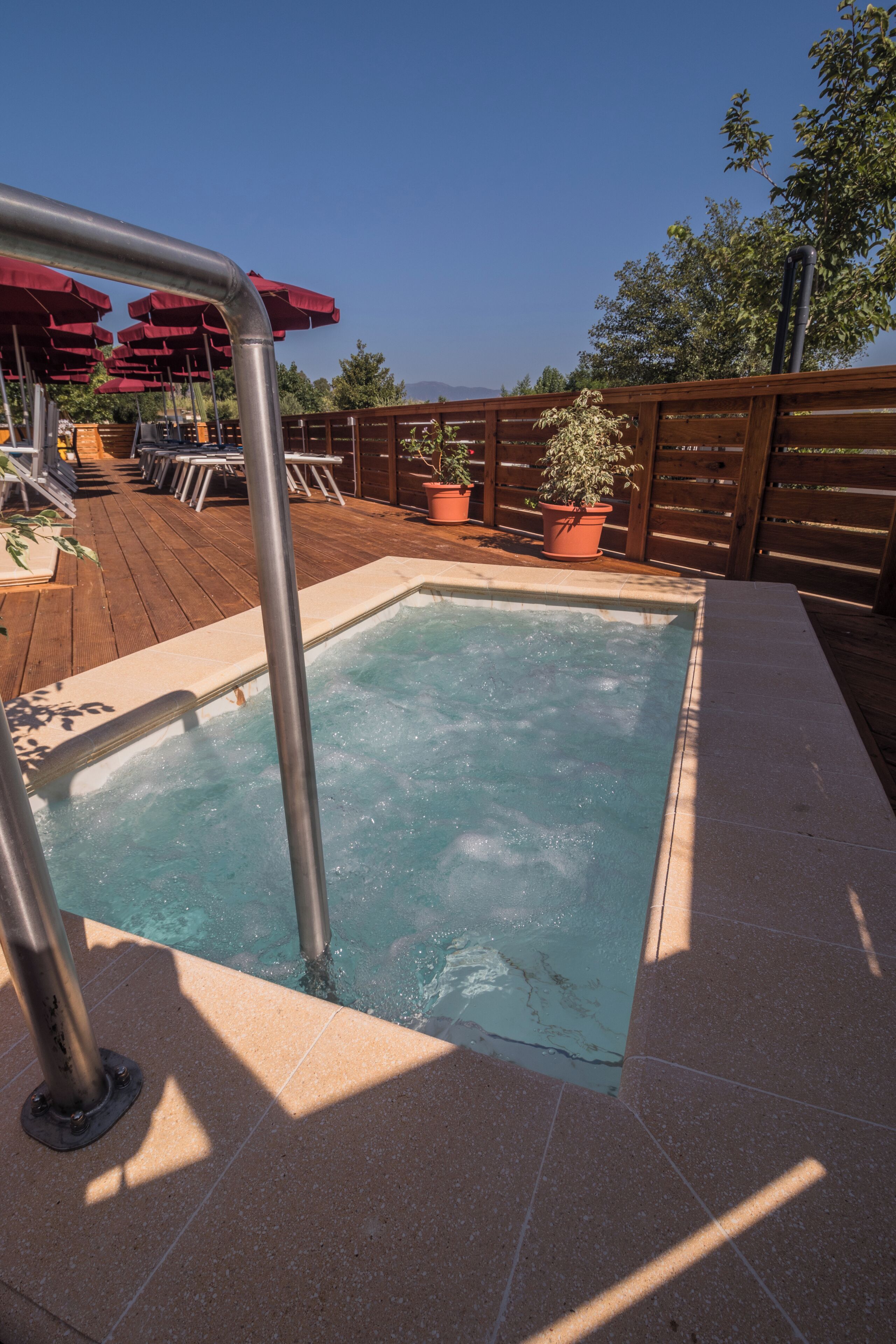 A hot tub with a wooden deck and potted plants.
