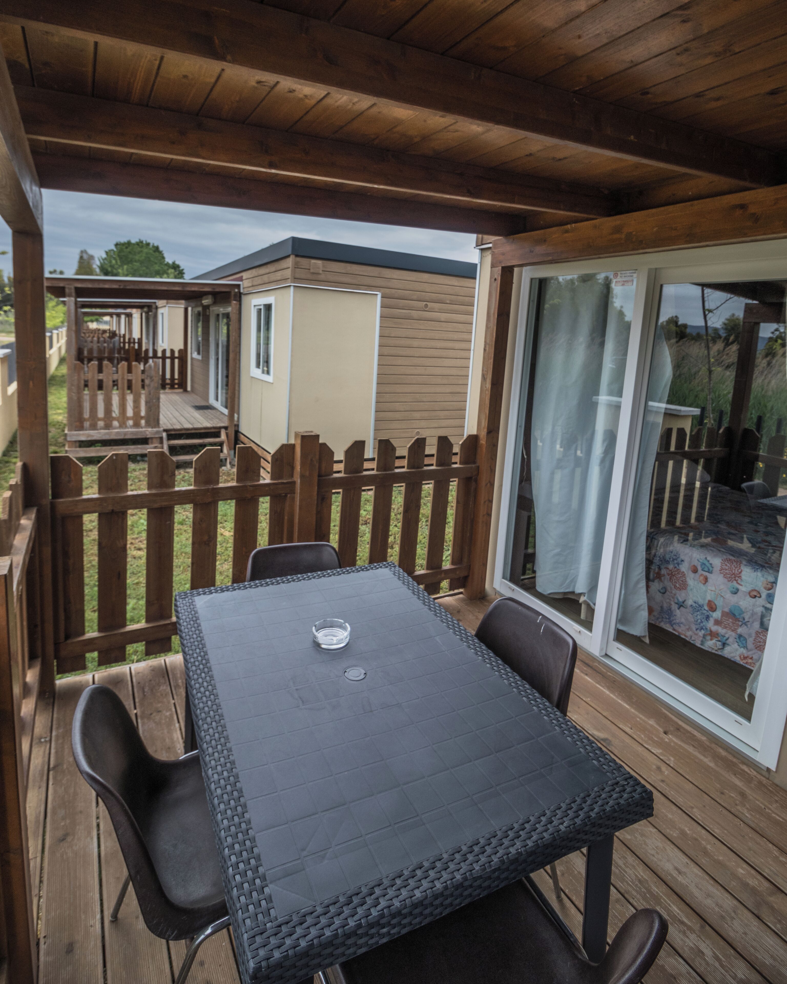 Eine überdachte Terrasse mit Tisch und Stühlen, ein Holzdeck und eine Glastür zum Garten.