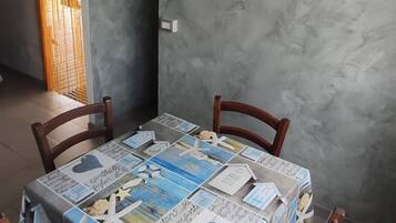 Un comedor con una mesa cubierta por un mantel estampado, cuatro sillas de madera, una lámpara en el techo y un equipo de aire acondicionado montado en la pared.