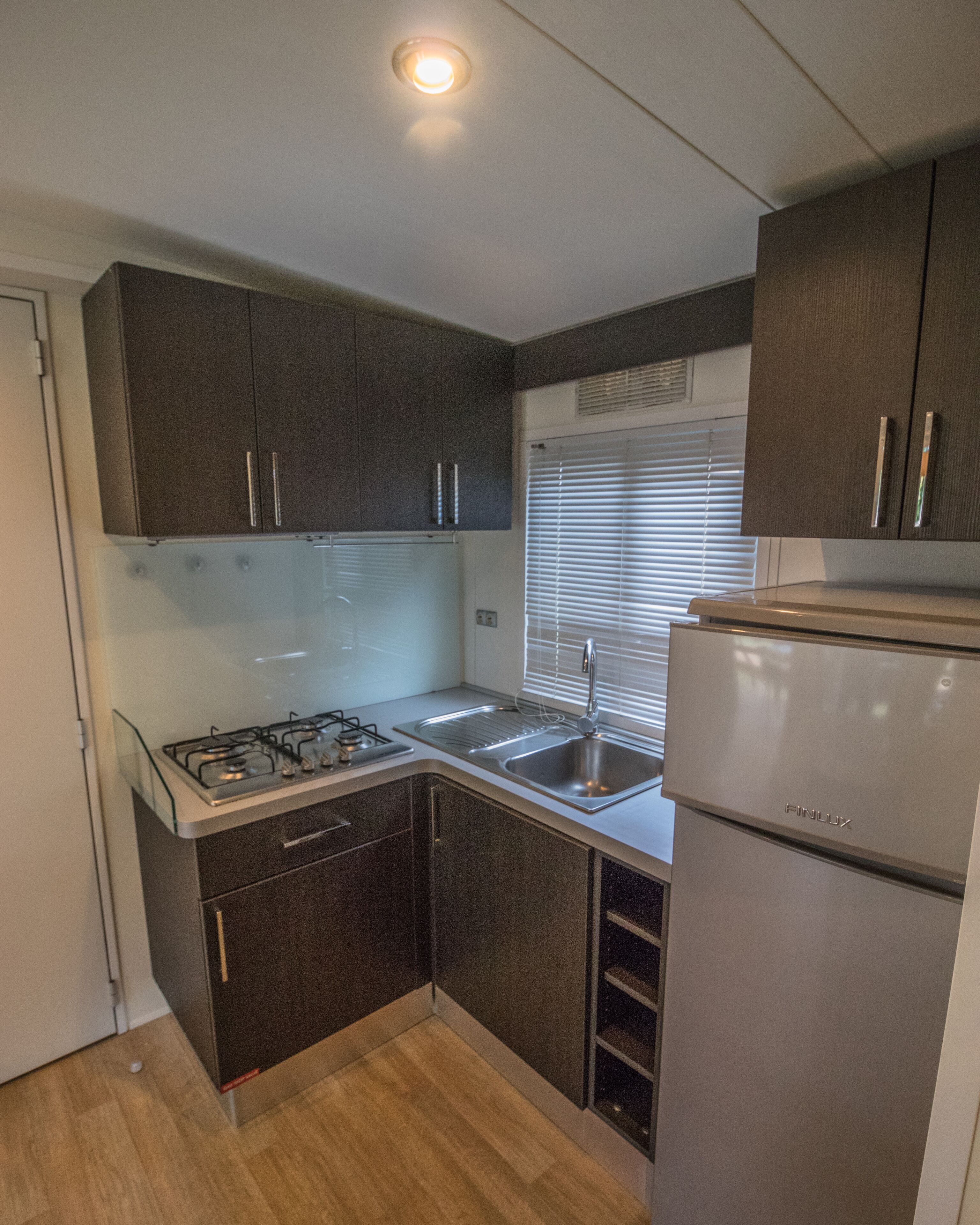 A compact kitchen with dark cabinets, a stainless steel sink, a gas stove, and a built-in refrigerator.