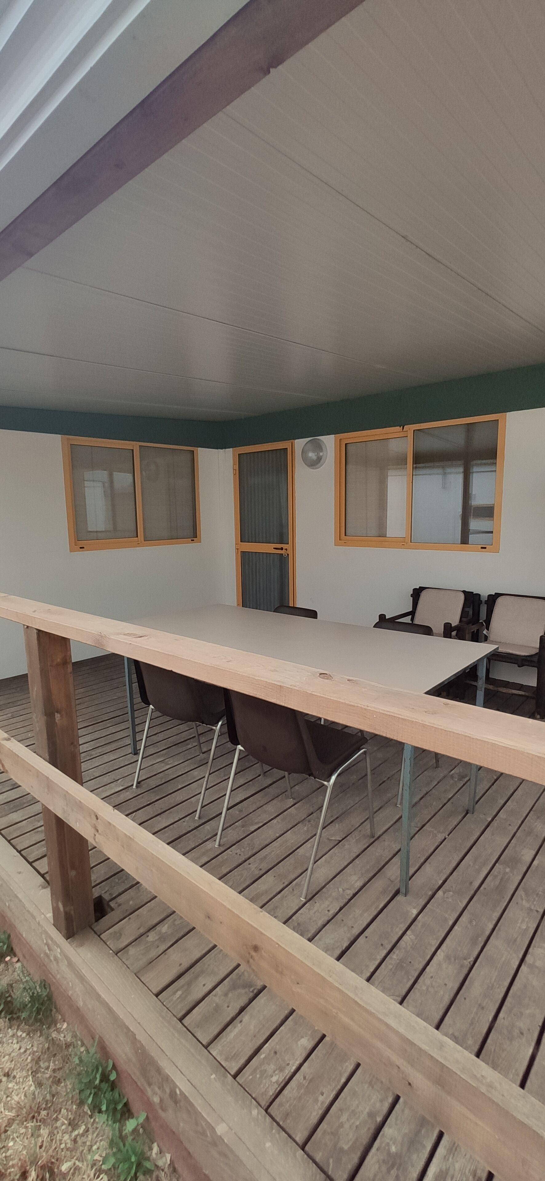 Een overdekt terras met een lange tafel, stoelen en een houten terras.