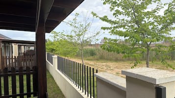 Un espacio al aire libre techado, con cerca de madera, pared de concreto y un árbol.