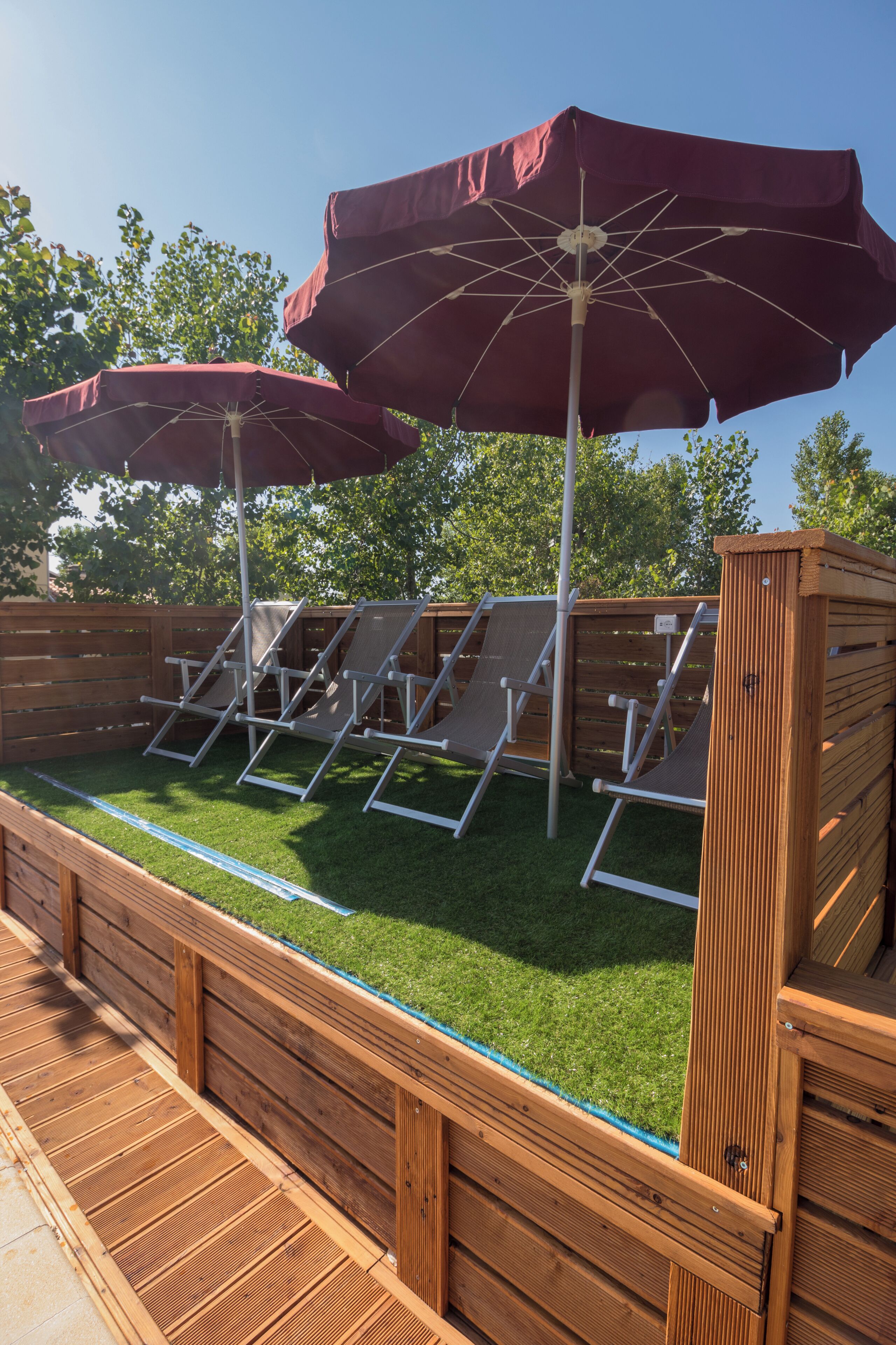 A pool area with wooden deck, lounge chairs, and two umbrellas.