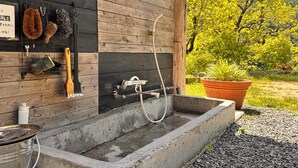 Une salle de bain extérieure rustique avec un mur en bois, un lavabo en béton et un tuyau d’arrosage.