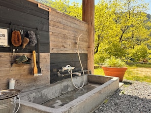 Un baño al aire libre rústico con pared de madera, un lavabo de concreto y una manguera.