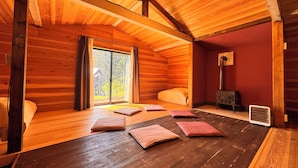 L’intérieur d’une cabane en bois, avec une grande porte coulissante donnant sur une terrasse, un radiateur et un lit avec des oreillers.