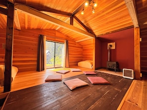 A wooden cabin interior with a large sliding door to a deck, a heater, and a bed with pillows.