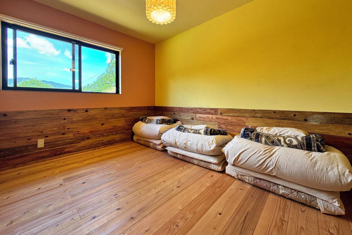 Une pièce dotée d’un plancher en bois, d’une grande fenêtre donnant sur un paysage verdoyant et d’un lit agrémenté de plusieurs oreillers.