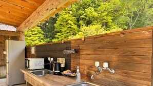Une cuisine extérieure rustique, dotée de plans de travail en bois, d’un évier, d’une bouilloire et d’un réfrigérateur.