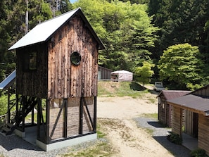 A rustic wooden structure with a sloped roof, a circular window, and a staircase leading up to a platform.