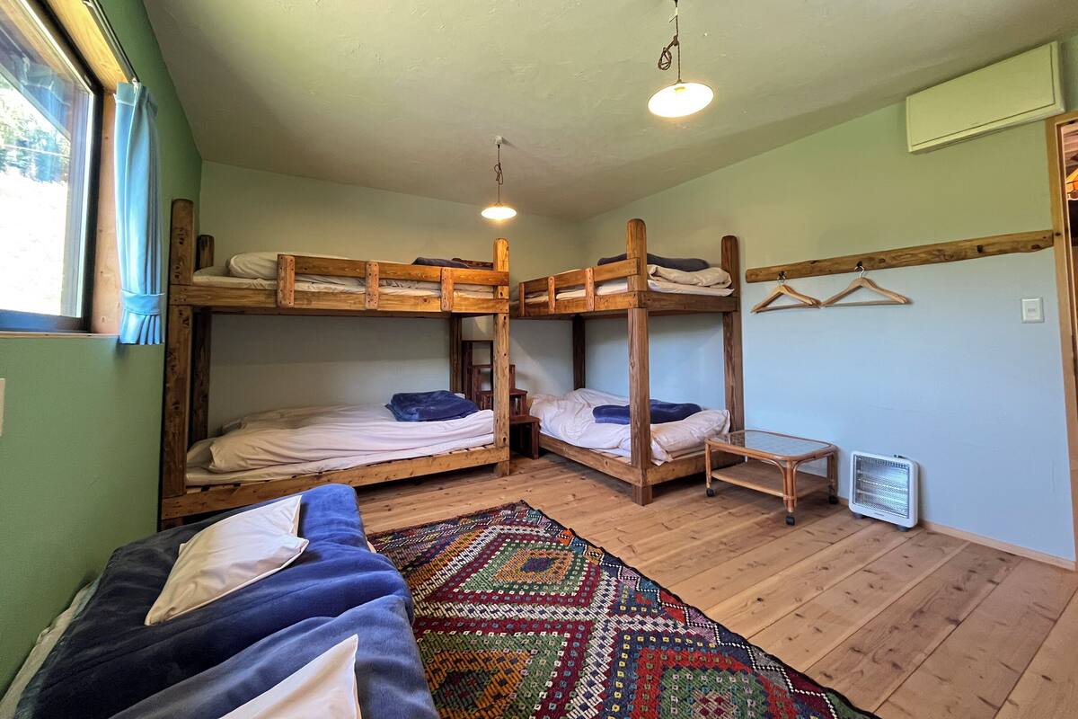 Une chambre avec un lit superposé, un luminaire suspendu, un petit radiateur et un tapis coloré.