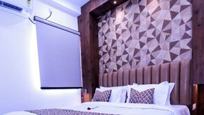 A modern hotel room with a large bed, geometric patterned headboard, and a white air conditioning unit on the wall. - The Commune KASHI (Varanasi)
