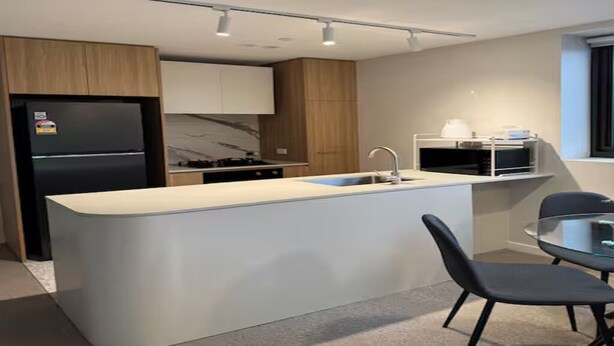 Uma cozinha moderna com ilha central, eletrodomésticos embutidos e espaço de jantar com cadeiras.