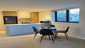 Uma cozinha moderna com uma ilha central, um espaço de jantar com mesa de vidro e cadeiras pretas, e uma janela grande que oferece vista para o exterior.
