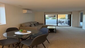 Uma sala de estar moderna com uma mesa de vidro redonda, um sofá e vista para área externa através de uma porta de vidro.