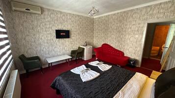 Ein Hotelzimmer mit einem Bett, einem Schreibtisch, einem Sessel, einem Fernseher und einem roten Sofa.