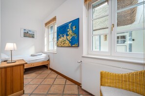 A bedroom with a bed, a nightstand, a lamp, a map on the wall, and a window with a view of the outside. - Urlaubshus, a thatched-roof vacation home in the seaside resort of Born (Born a. Darß)