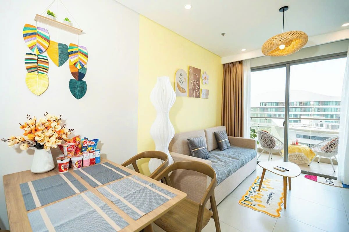 Un salon moderne avec un canapé, une table à manger et des chaises. Une grande fenêtre offre une vue sur les bâtiments.