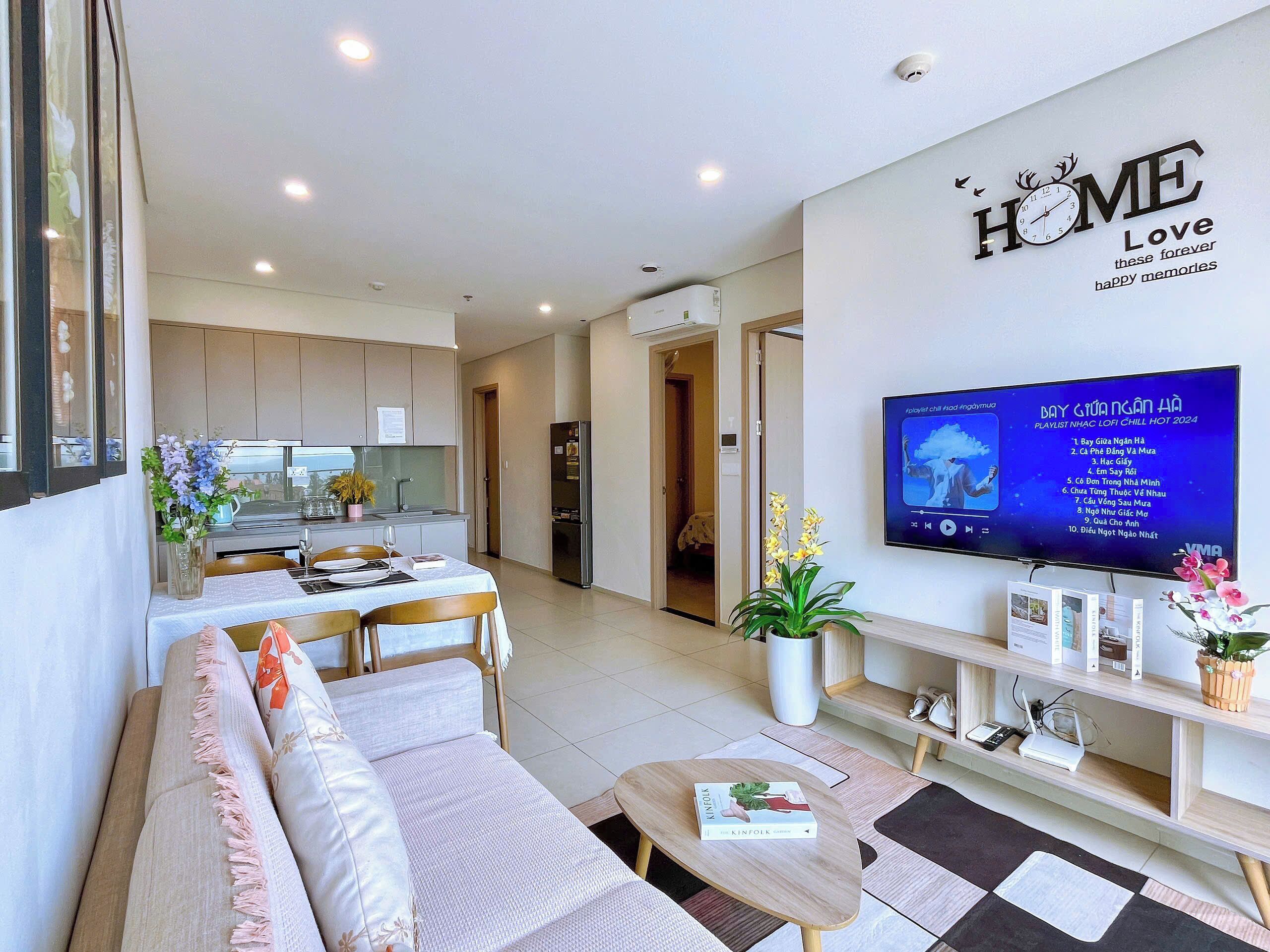 A modern living room with a sofa, coffee table, and a TV mounted on the wall displaying a music playlist.