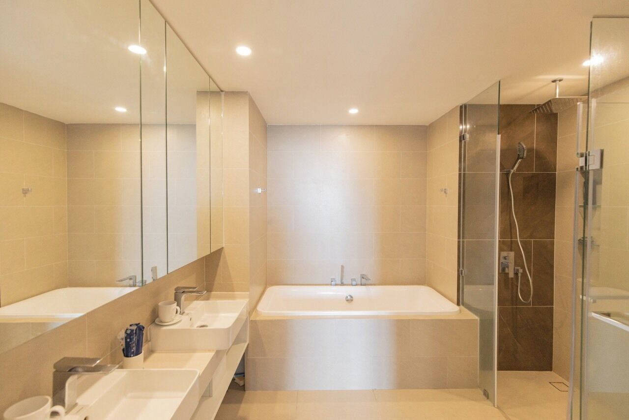 A modern bathroom with two sinks, a bathtub, and a glass-enclosed shower area.