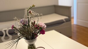 Et hvidt bord med en vase blomster i et moderne rum med en grå sofa og hvide vægge.