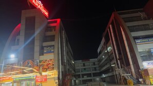 Un hotel llamado Paradise con un letrero rojo llamativo, un letrero de Shree Nath Real Estate y una escalera visible que conduce a los pisos superiores.