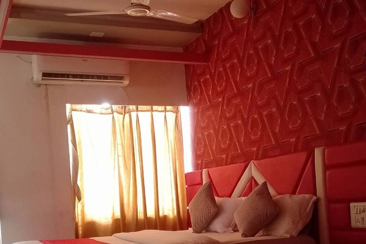 A modern bedroom with a red and white color scheme, a bed with multiple pillows, a ceiling fan, and an air conditioning unit.