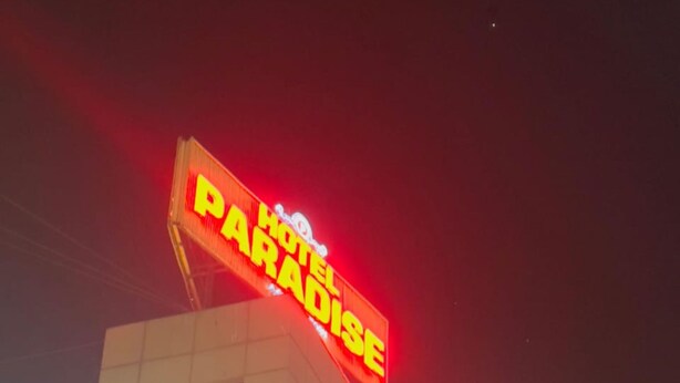 Un cartel de hotel con el nombre 'Hotel Paradise' y un anuncio de bienes raíces debajo.