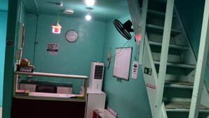 A reception area with a counter, a clock, a fan, and a staircase. - Wind Stay (Malé)