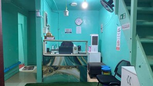 A small, teal-colored room with a desk, chair, and a clock on the wall. - Wind Stay (Malé)