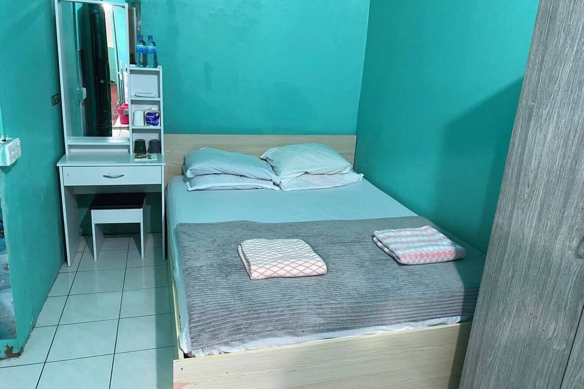 Une petite chambre avec un lit simple, une tête de lit en bois, une table de chevet, un miroir et une armoire.