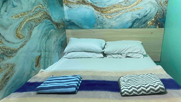 A bed with a striped blanket and a chevron pillow, a wooden headboard, and a wall with a marble-like pattern. - Wind Stay (Malé)