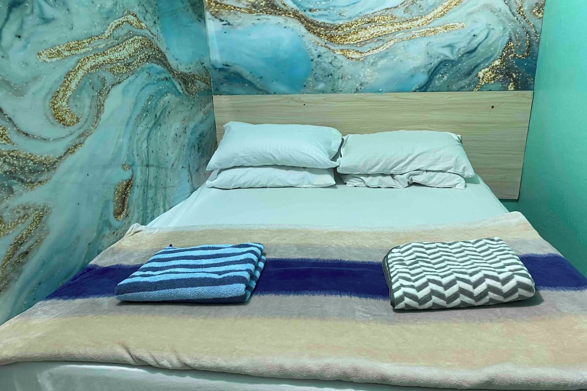 Un lit avec une couverture à rayures et un coussin à motifs chevrons, une tête de lit en bois et un mur orné d’un motif rappelant le marbre.