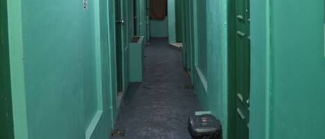 A narrow hallway with green walls and doors, a trash bin, and a ceiling light.