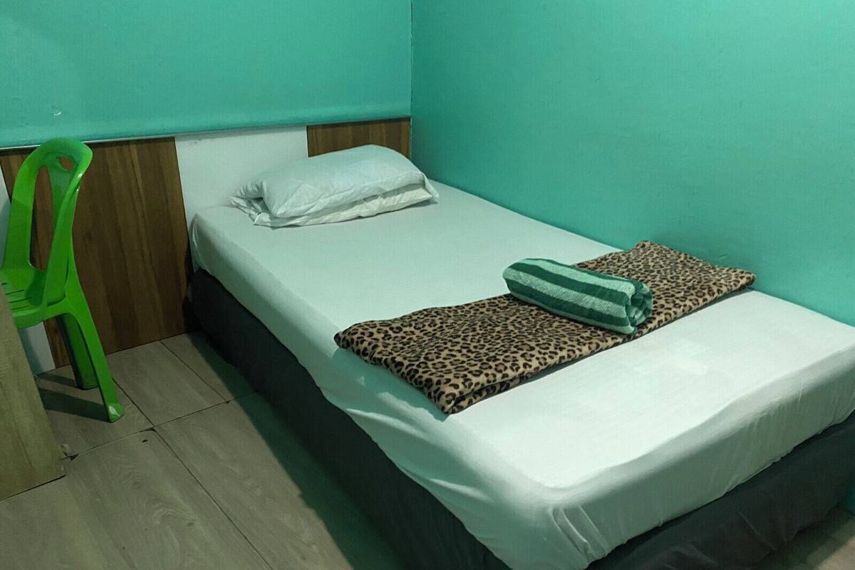 Une chambre avec un lit simple, une tête de lit en bois, une chaise en plastique verte et une couverture à motifs léopard.