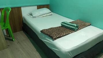 Habitación individual con una cama de madera, una silla de plástico verde y una manta de estampado de leopardo.