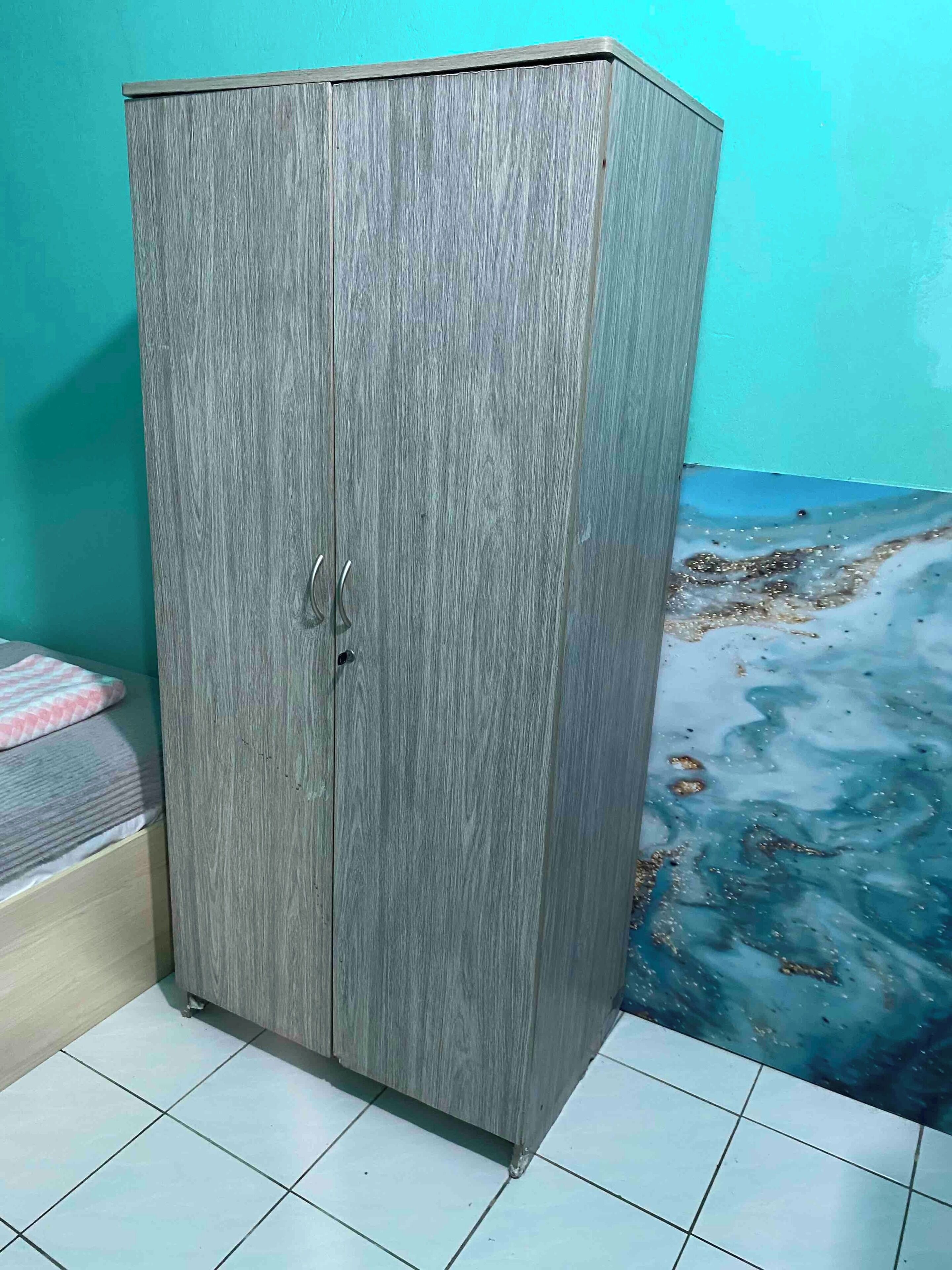 Une armoire à la surface texturée, un lit recouvert d’une couvre-lit à motifs et un sol carrelé.