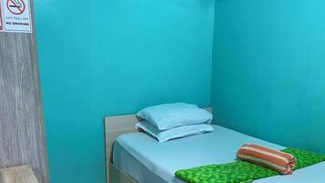 Una habitación pequeña con cama individual, pared azul, piso estampado, cartel de no fumar y aire acondicionado.