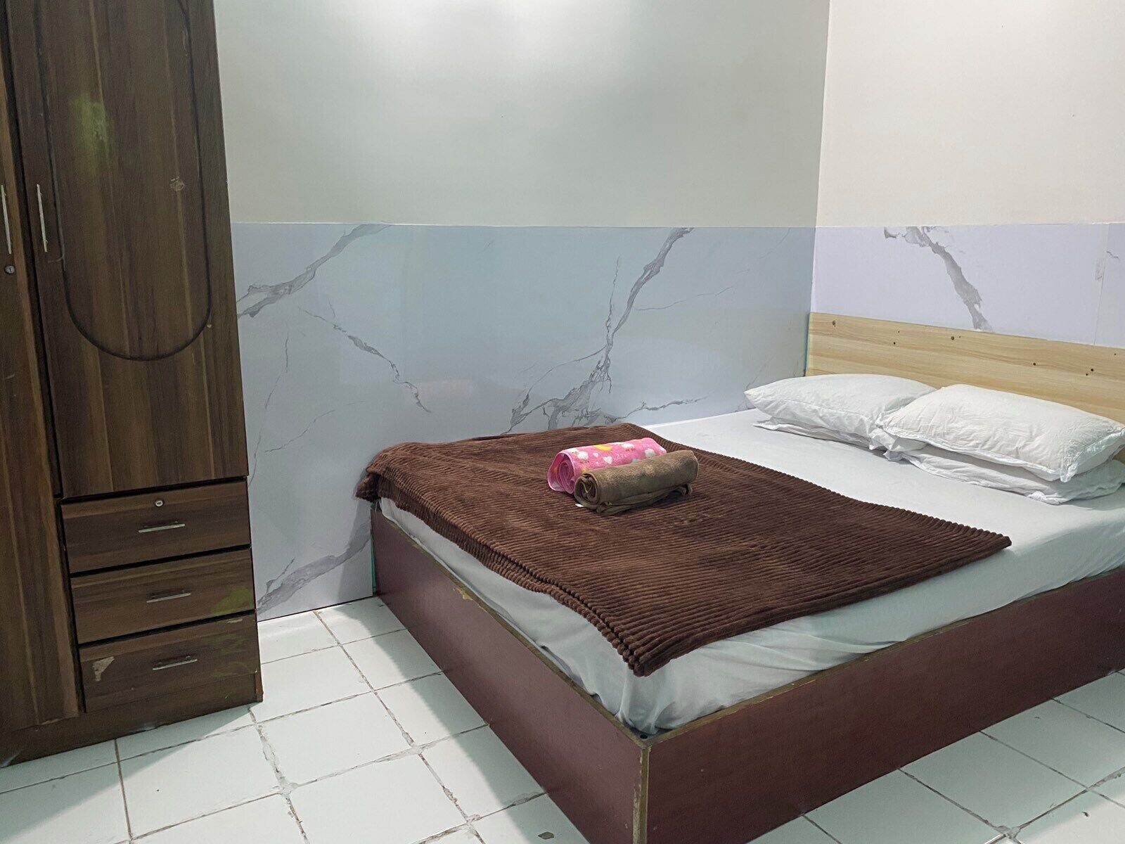A bedroom with a bed, a wooden wardrobe, and a marble-patterned wall.