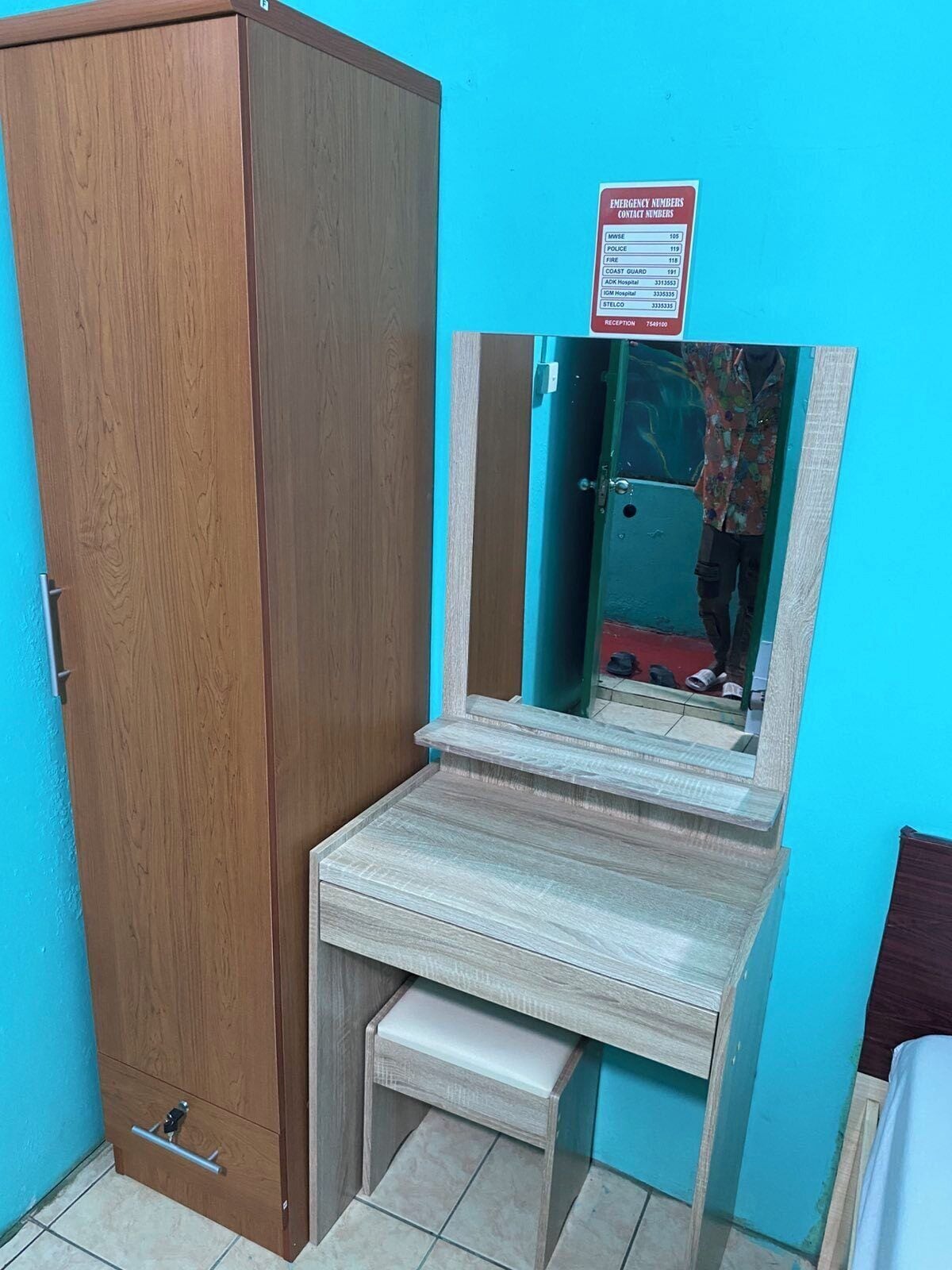 A room with a wooden wardrobe, a small desk with a mirror, and a blue wall.