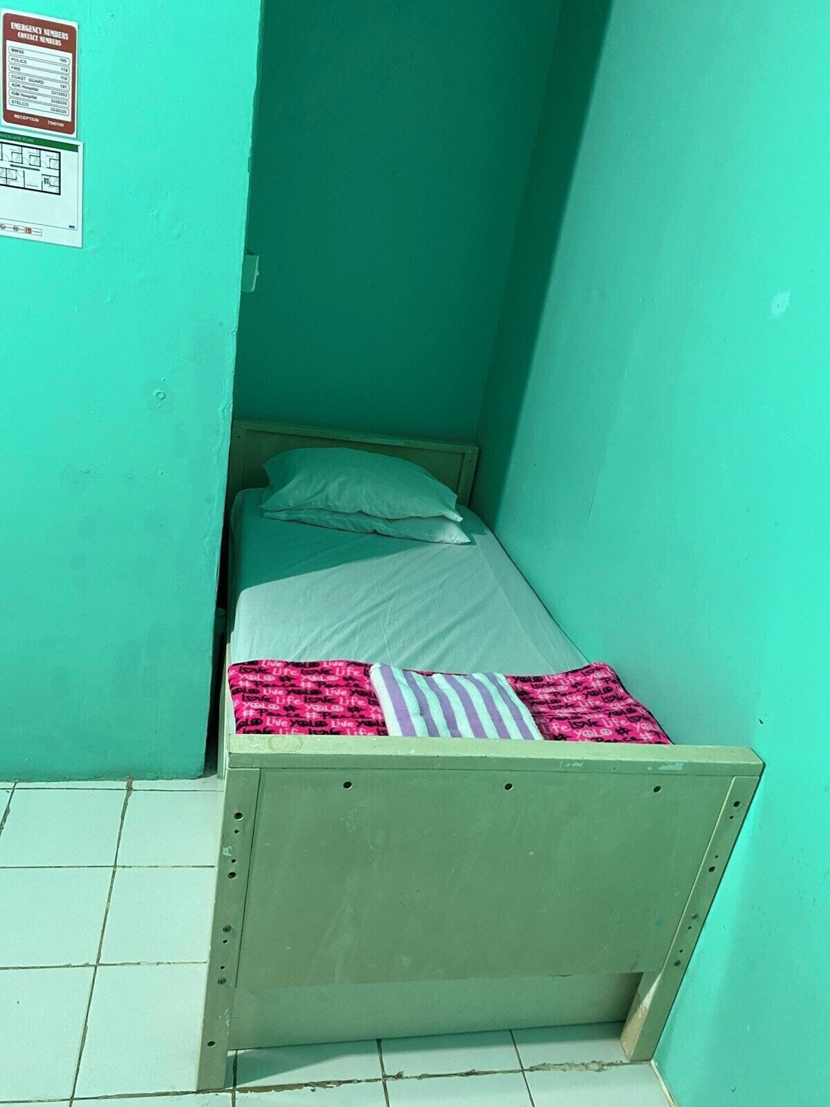 A small, single-bed room with teal walls and a tiled floor.