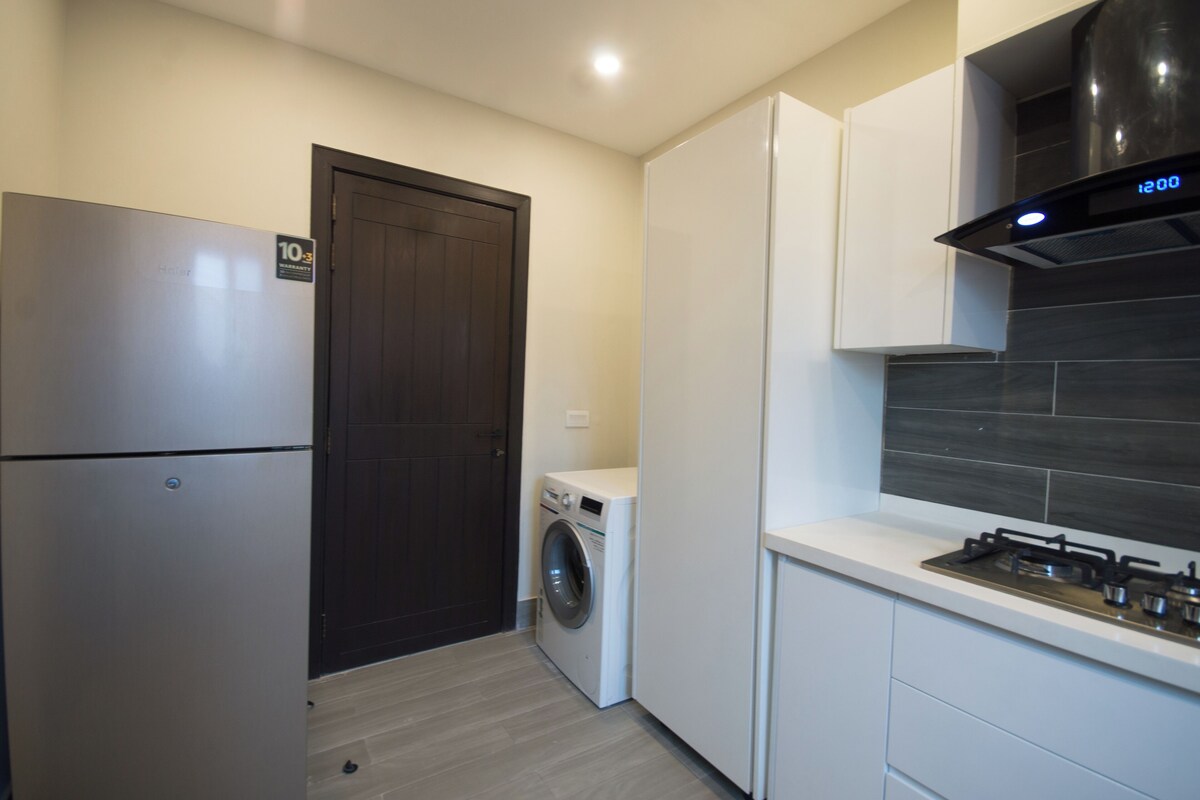 Una cocina compacta con un refrigerador de acero inoxidable, una lavadora y una estufa a gas.